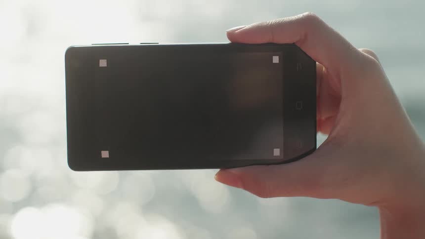 A woman holds a cell phone up outside