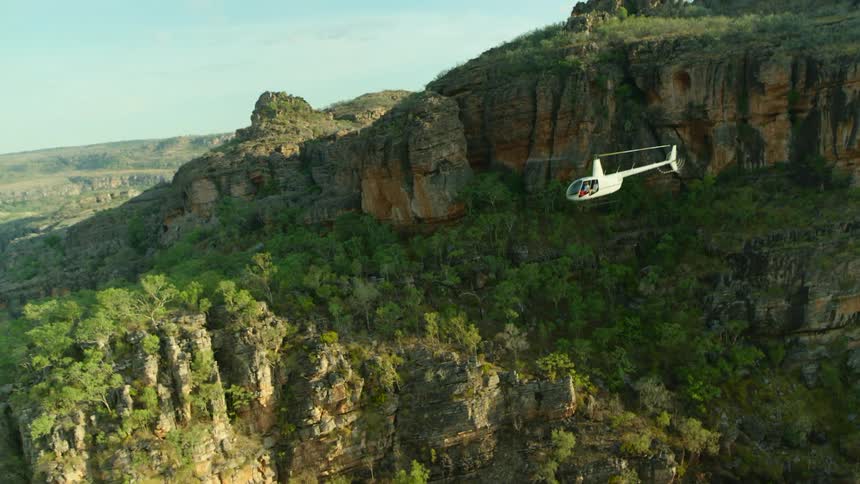 A helicopter is flying over mountains on a sunny day