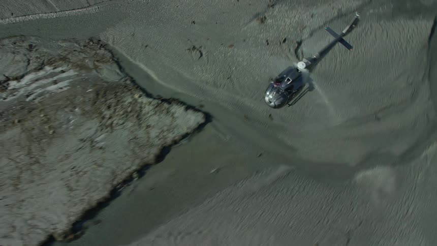 An aerial view of a helicopter flying over a coastal region with sand and rocks during the day