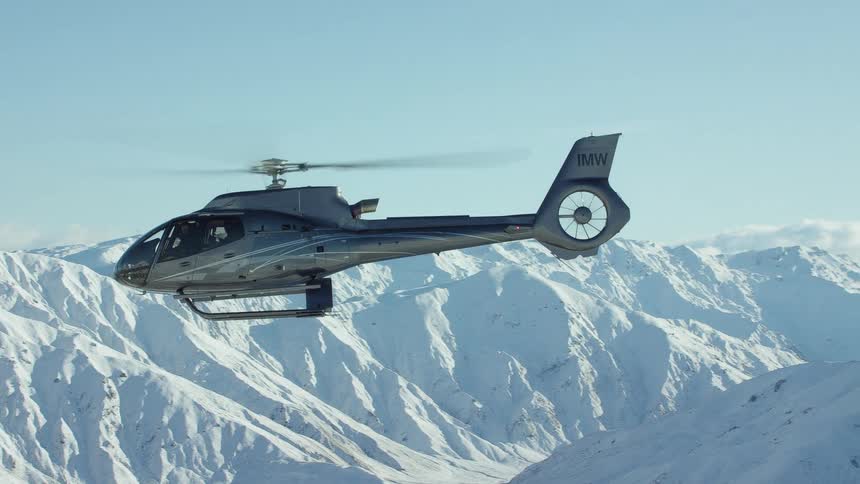 A helicopter is flying near snow covered mountains