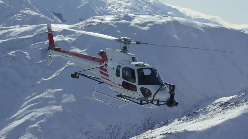 A helicopter is flying near snow covered mountains