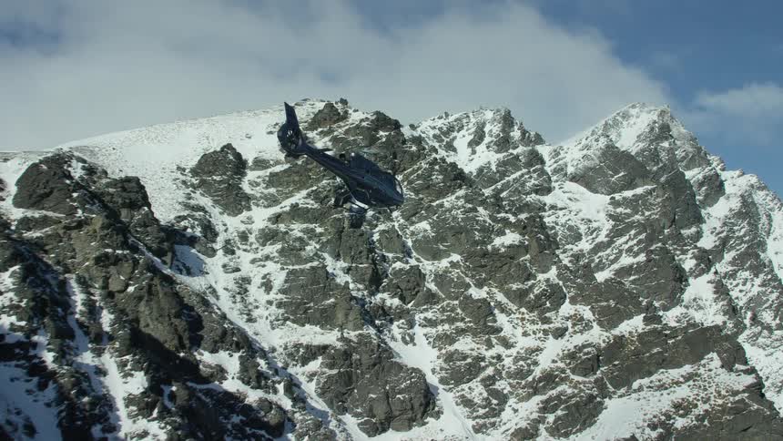 Helicopter flies over high snowy mountains