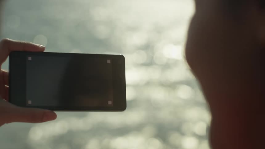 Two teenagers aboard a boat enjoy recording the ocean with a smartphone during the day