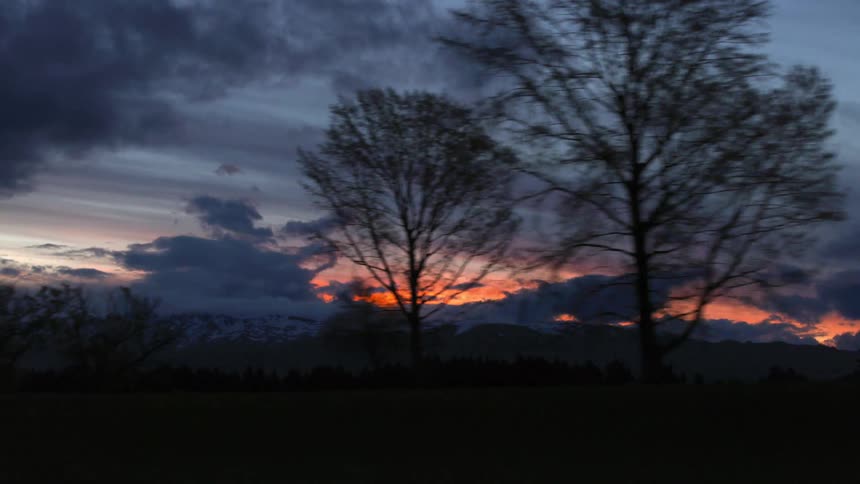 A camera moves left along a landscape of the sky and trees at dawn or dusk
