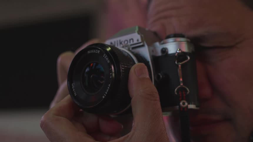 A man adjusts the focus of a nikon camera while looking through it to take a photo