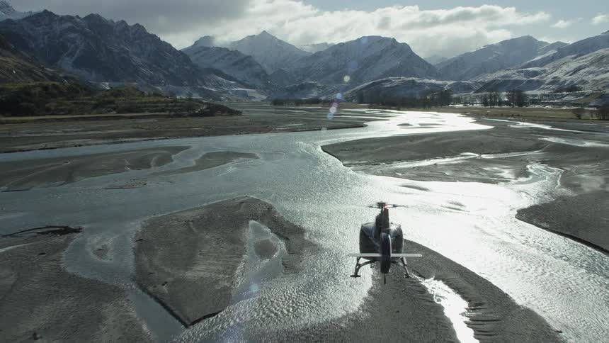A helicopter flies over a river and creek that leads to a mountain range