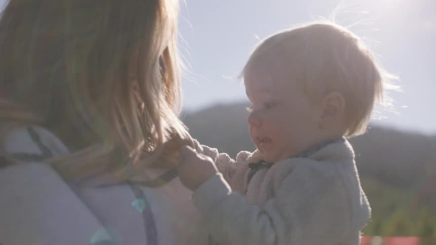A woman stands outside and holds a young boy in her arms