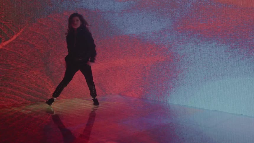 A girl dancing in a room with a screen on the walls in the background