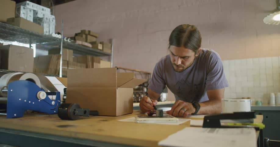 Man writes with a pen on a piece of paper while leaning against a table in an office