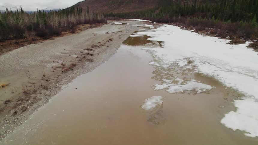Snow and ice on a river near a forest and mountains