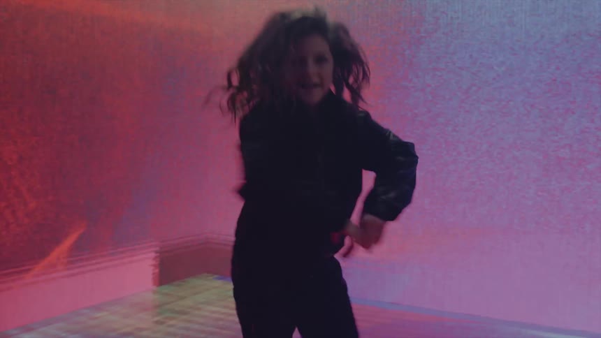 A girl dancing in a room with a screen on the walls in the background