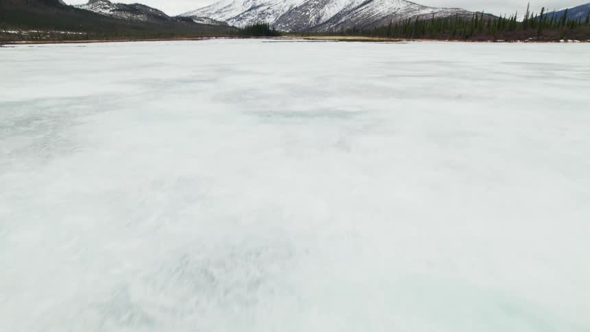 Frozen lake leads through forests to snowy mountain under overcast sky