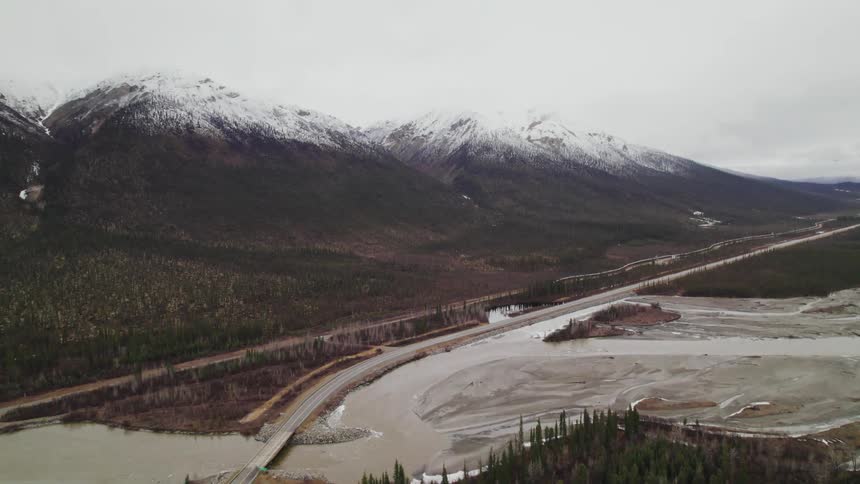 An aerial view of a river and road near a snowy mountain range in winter