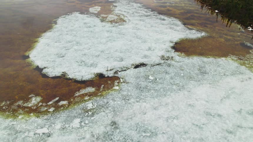 An aerial view of an icy body of water in front of a mountain in winter