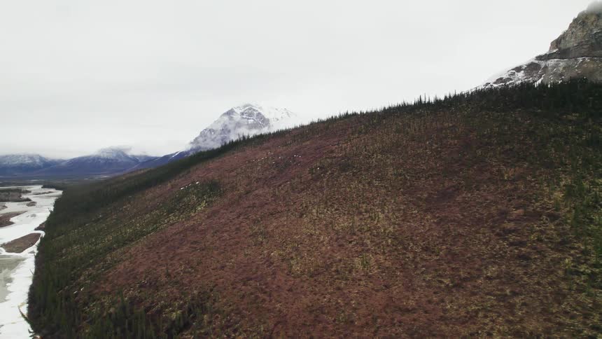 Snow at the base of a hill and on the mountains