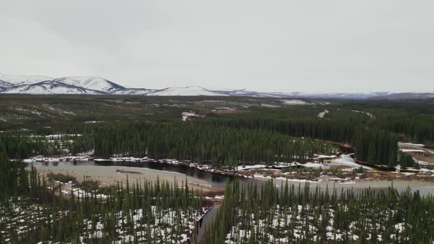 A river runs through snow covered mountain and forest wilderness