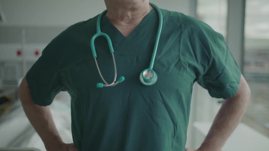A doctor is standing in his office next to a window