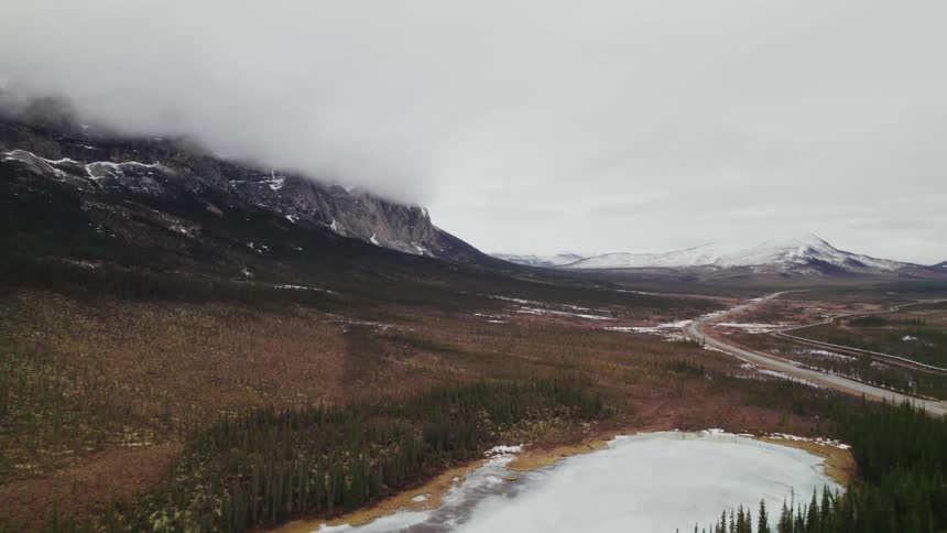 A landscape with trees a road and ice with a mountain range the sky and clouds in the background