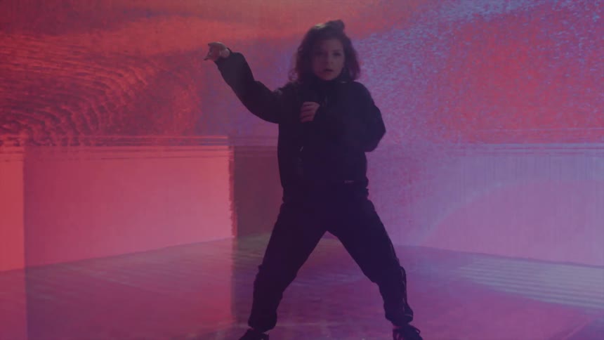 A young girl dances hip hop in front of a digital screen with colorful graphics