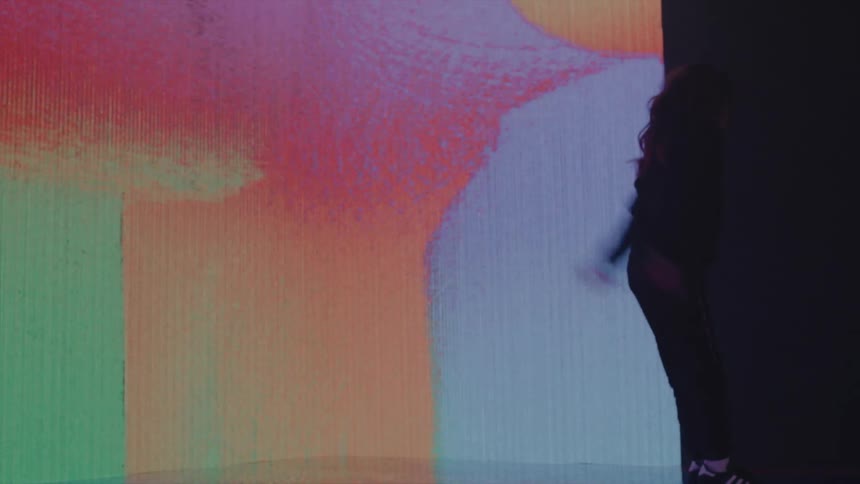 Young female dancer dances and flips on stage against digital screen walls showing various colors and images