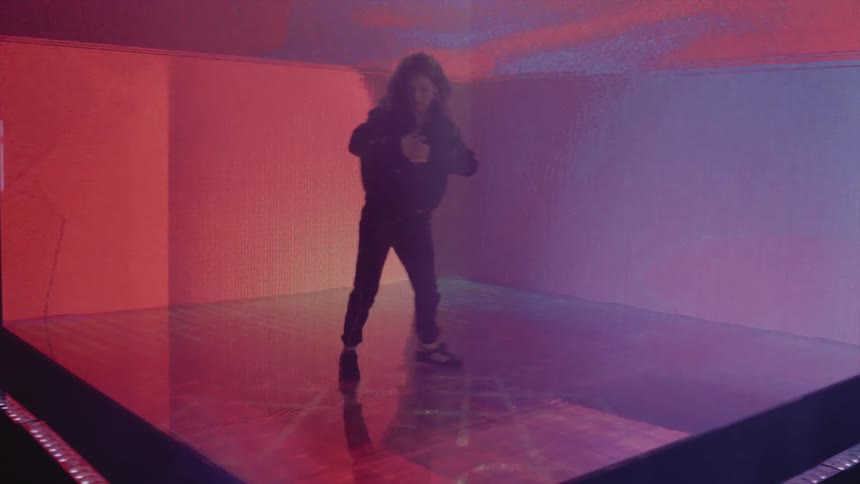 Teenage girl dances on stage surrounded by large wall screens showing various colors and patterns