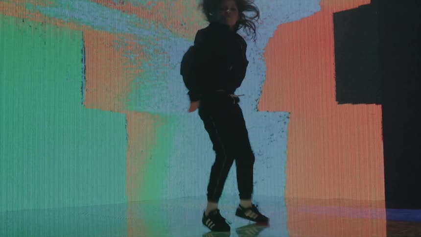 Girl energetically dancing on stage in front of an abstract colorful digital display