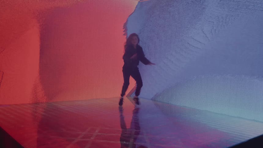 A young girl dances hip hop in front of a colorful electronic display