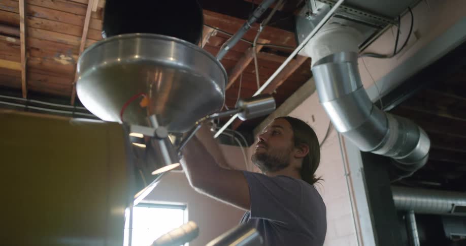 A man pours the contents of a bucket into a machine in a manufacturing facility