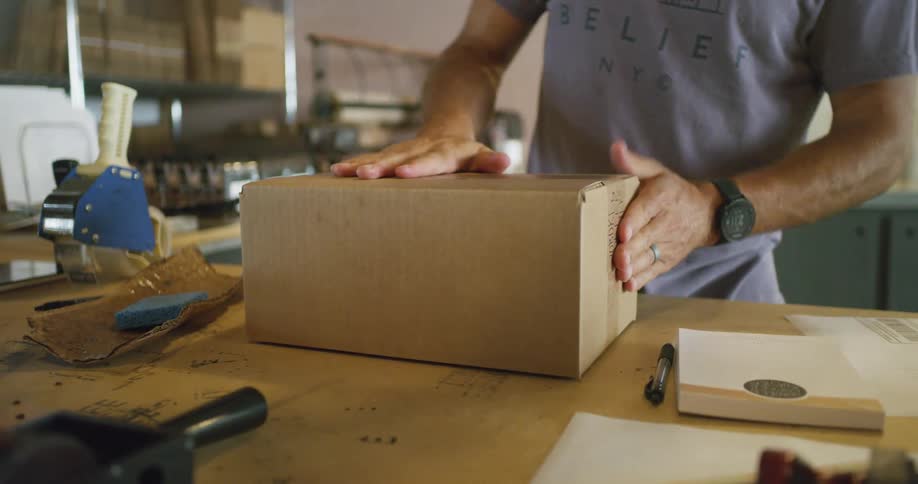 A man smoothes the tape on the outside of a cardboard package