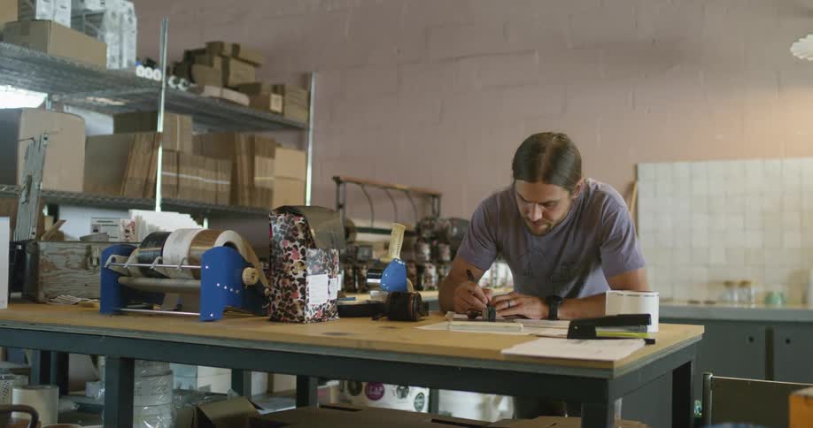 A man standing at a work table begins to fill out a shipping label