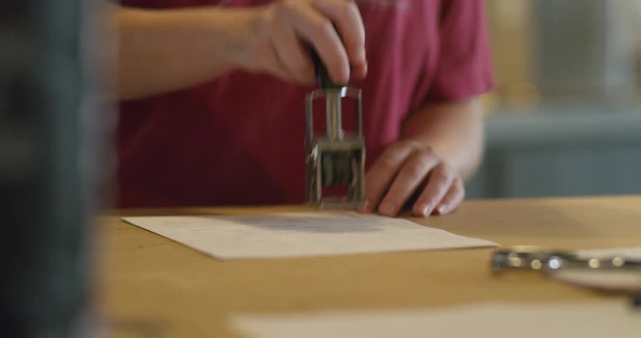 Clerk stamping a paper form with a ink stamp over a desk