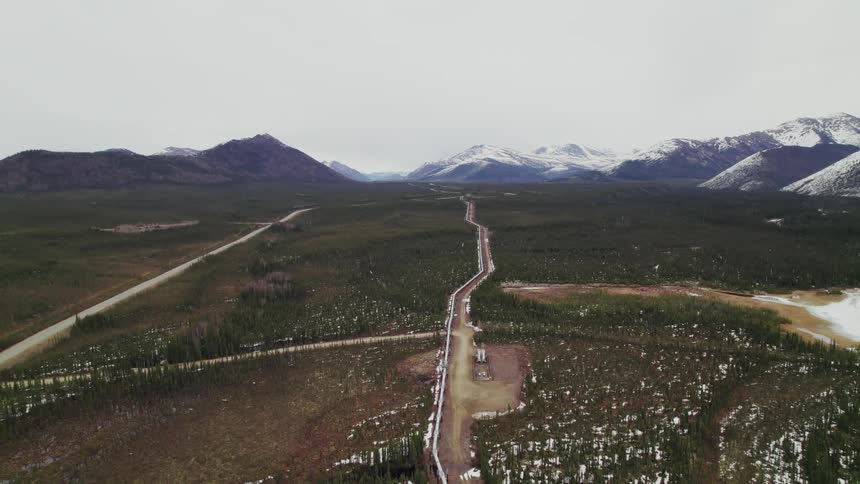 Roads and pipeline through rural area with a nearby lake and mountains in the distance