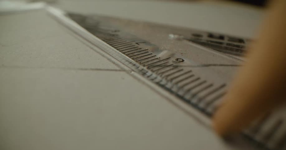 A pencil drawing a line against a ruler on a piece of paper
