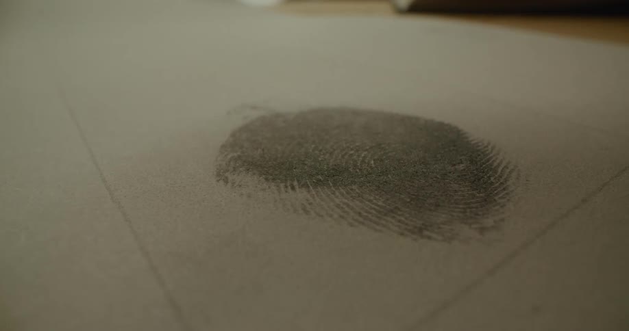 A person presses their finger onto a sheet of paper leaving an ink fingerprint