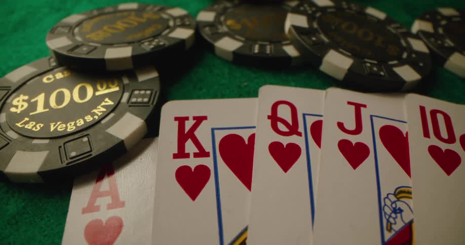 One hundred dollar casino chips are tossed next to a straight flush hand