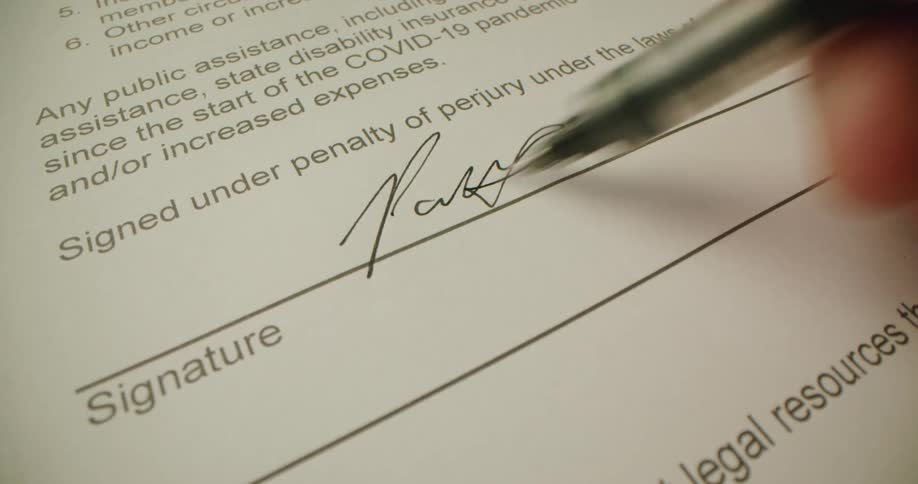A person signs a government assistance form with a black ink pen