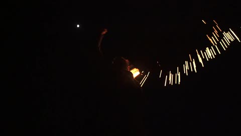 A man is spinning fire in a night sky