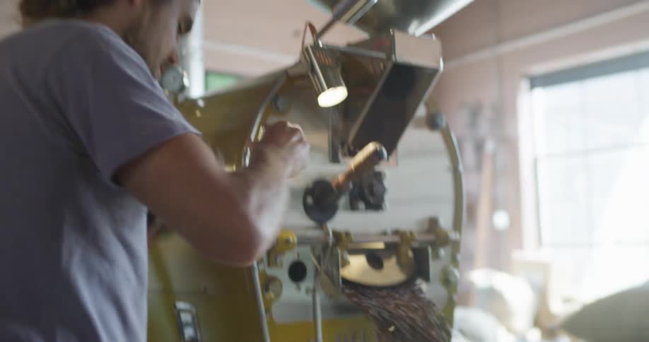 Man operates coffee roasting machine briefly smelling product and wiping machine