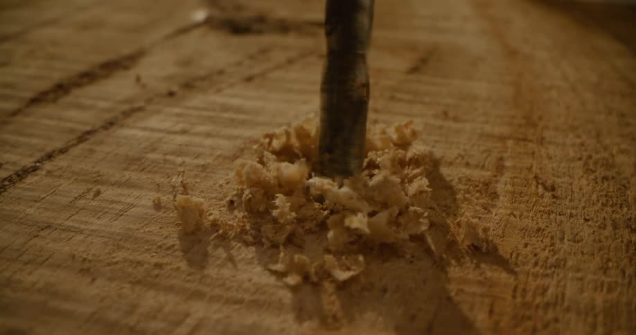 A drill drilling wood and wood chips falling on the wood
