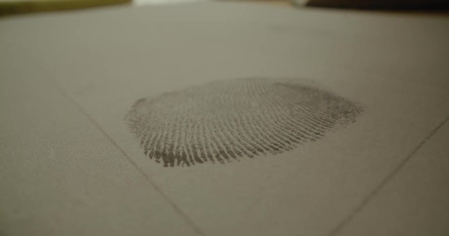 Person presses ink stained finger onto paper making a fingerprint