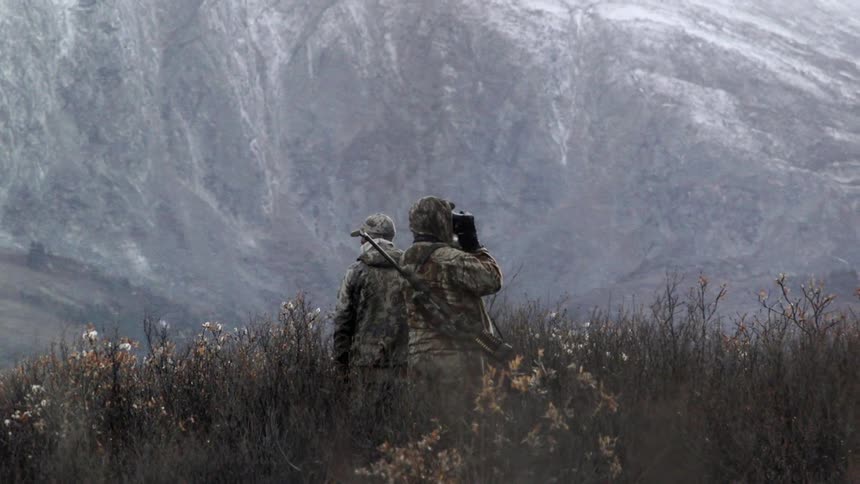 Two people look around outside in the snow next to a mountain