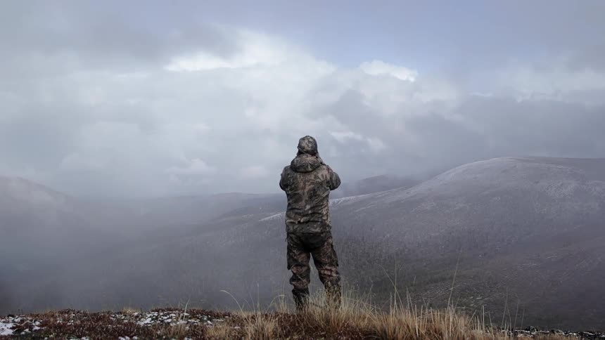 A man stands on a hill as a bird flies past
