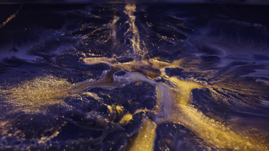 golden streams of paint flow and spread in macro on a piece of paper
