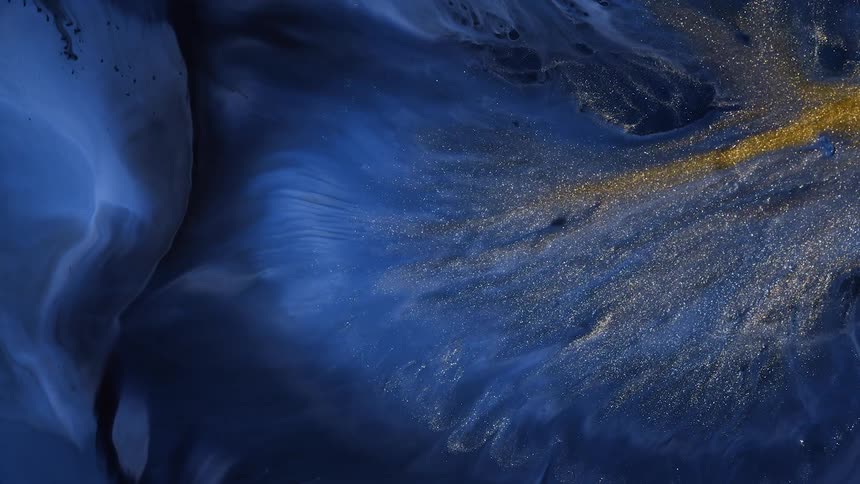 Glitter powder spreads across surface of swirling flowing blue and gray paint