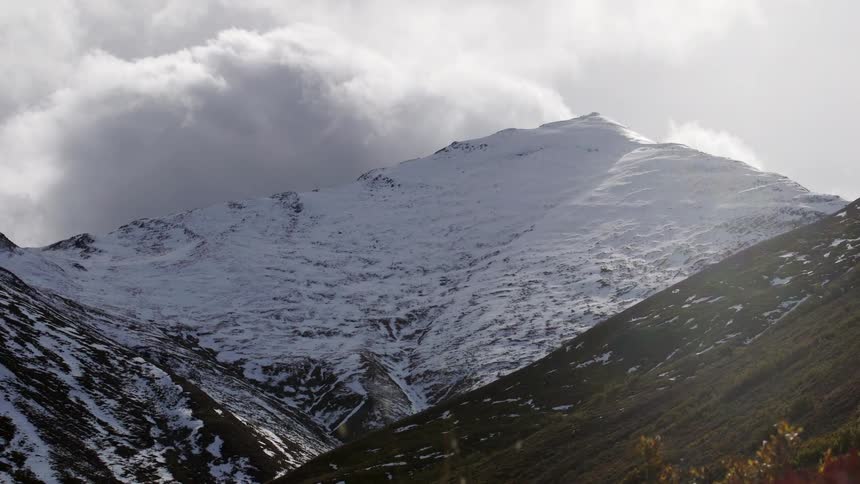 Clouds passing behind a snowy mountain