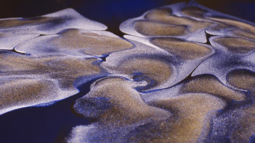 Purple and blue mixture surrounds golden brown areas both covered in golden sparkles as they flow
