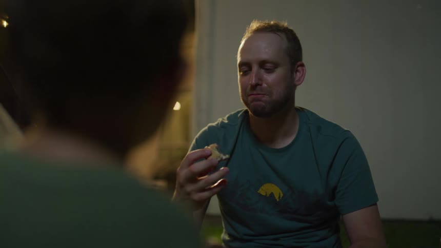 A man and boy sit outside at night eating smores
