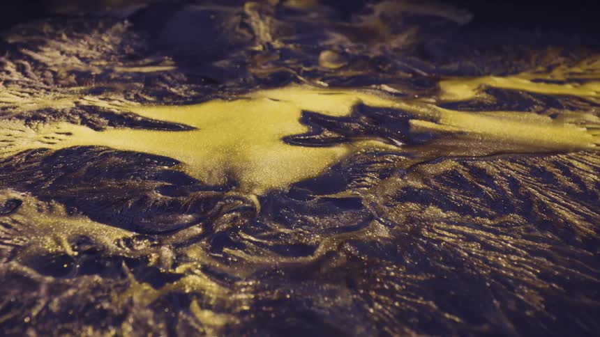 Glittering gold particles spread over mounded blue and purple dye as they spread and flow