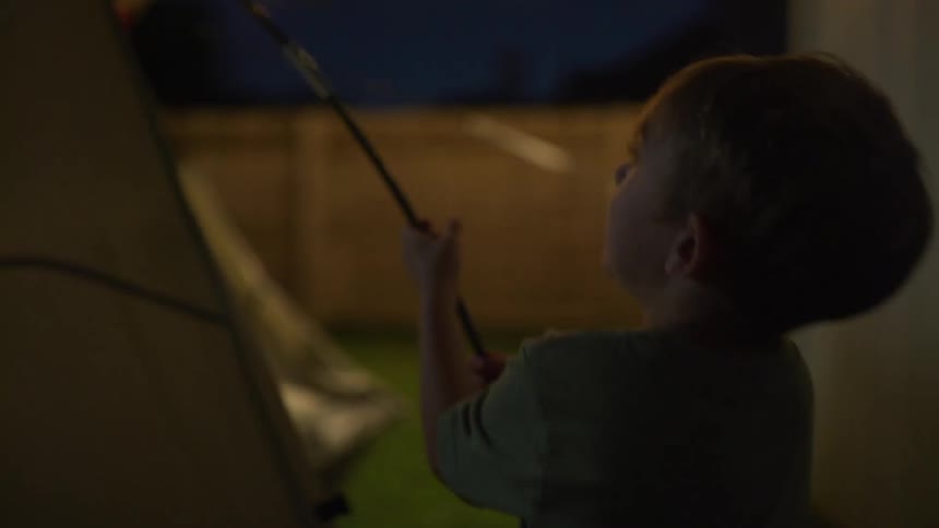 A father and young son setting up a tent in a backyard on a summer evening
