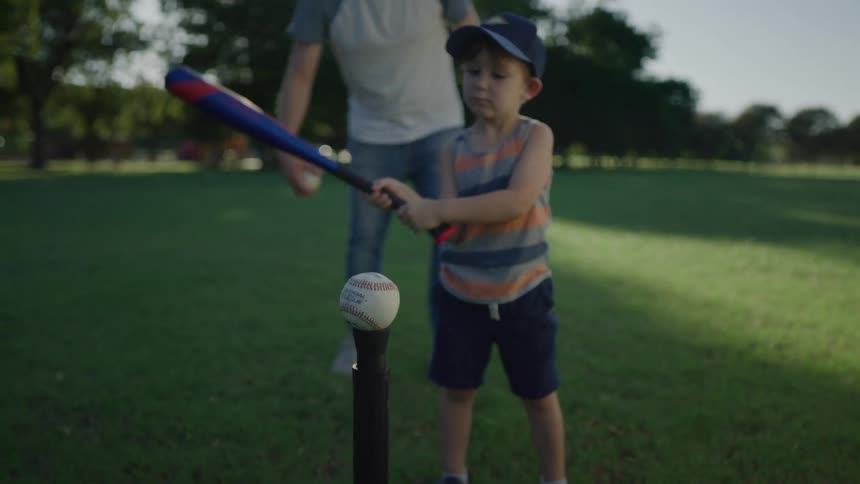 Father teaches his son to hit a ball on a tball stand